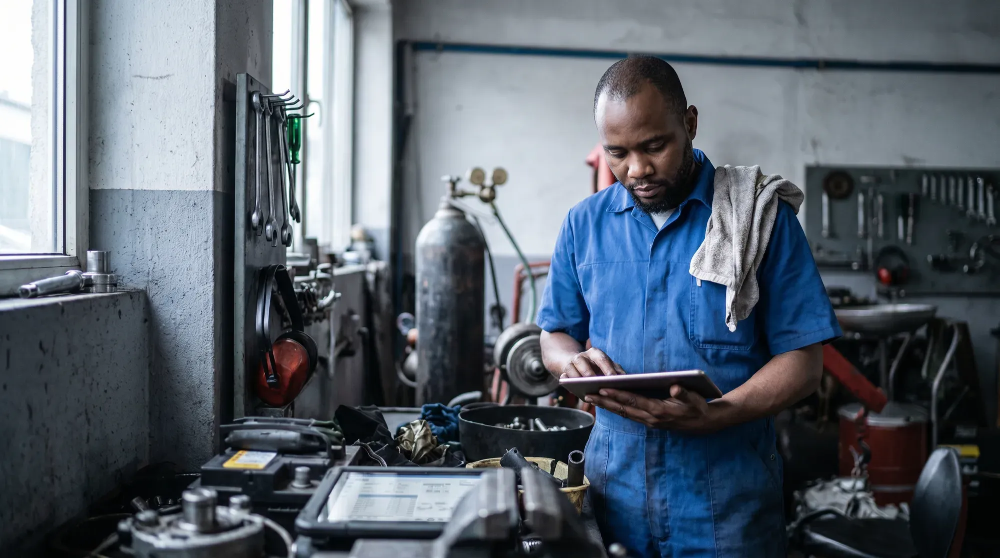Mechaniker in blauer Arbeitskleidung liest in einer Werkstatt eine Anleitung auf einem Tablet